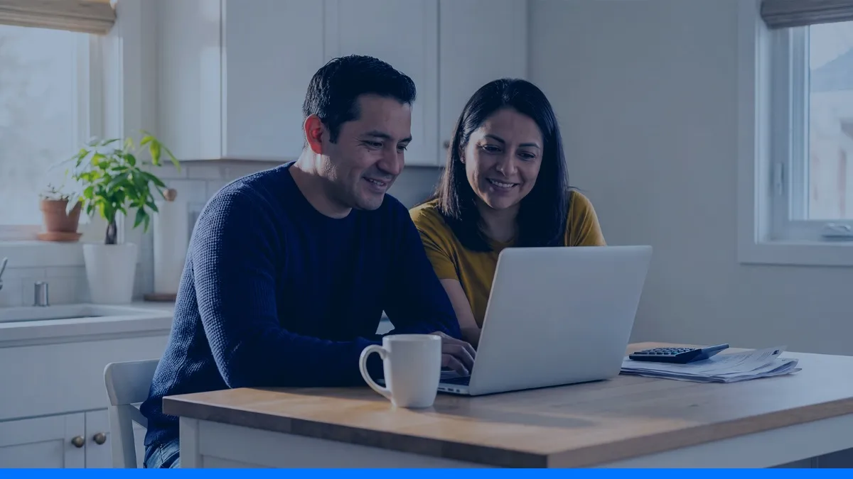 Casal sorri diante do notebook na mesa da cozinha, como quem consulta o precatório TJRN no SIGPRE.