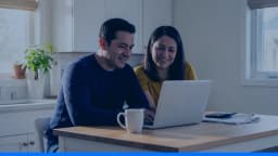 Casal sorri diante do notebook na mesa da cozinha, como quem consulta o precatório TJRN no SIGPRE.