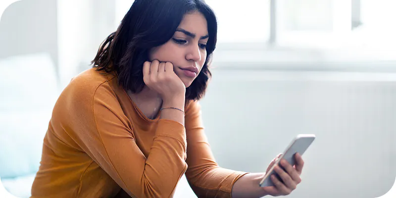 Mulher pensativa segurando o celular, ilustrando a demora da fila do precatório