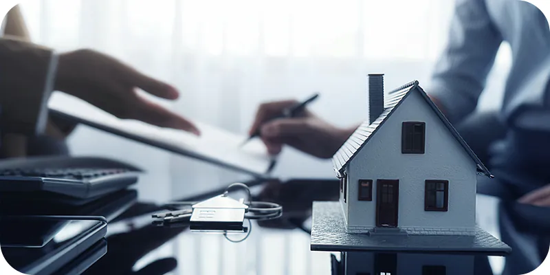 Miniatura de casa e chaves no primeiro plano, assinatura de documento em segundo plano, representando comprar imóvel com precatório